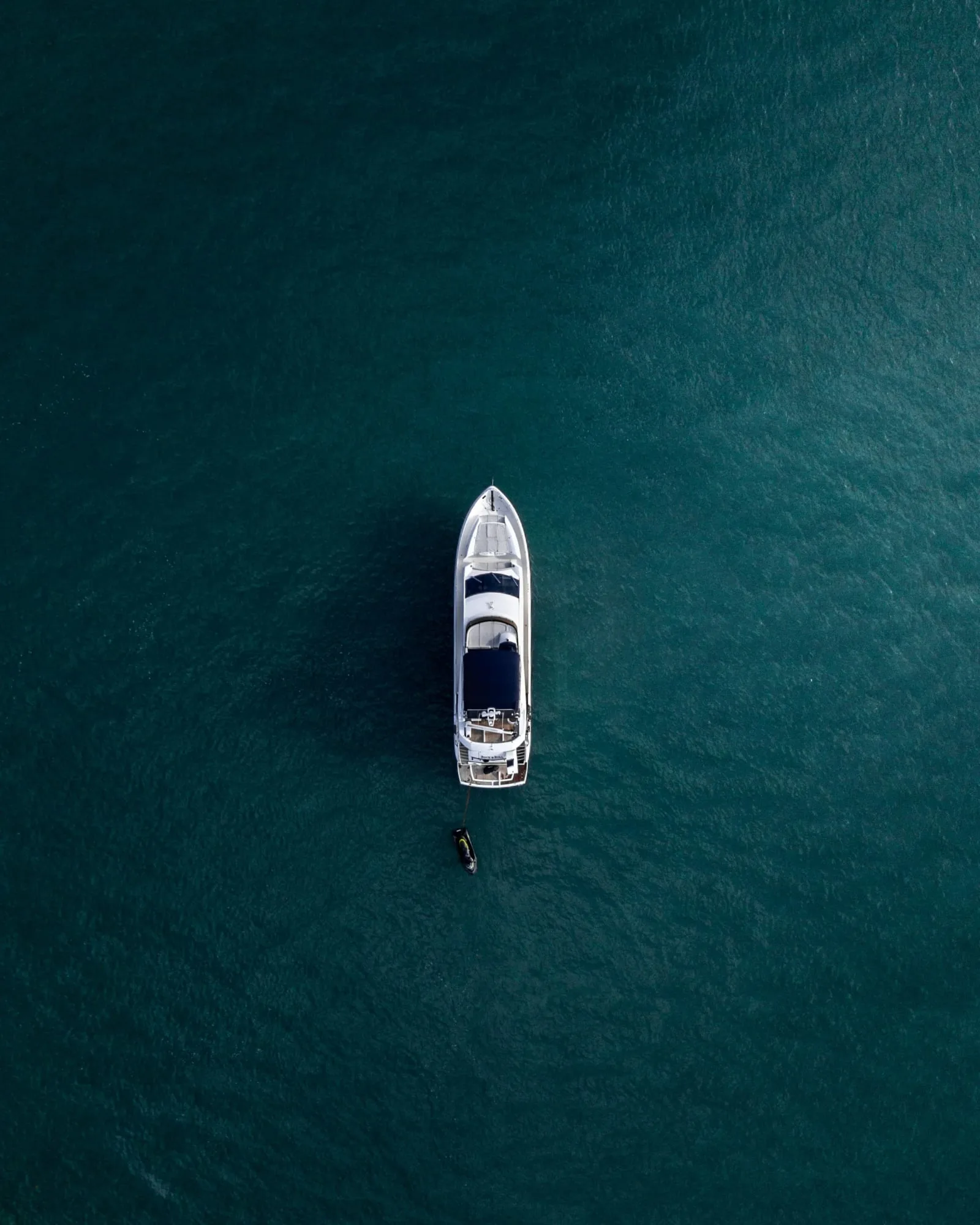 Aerial view of a yacht on calm blue water with a small boat nearby.