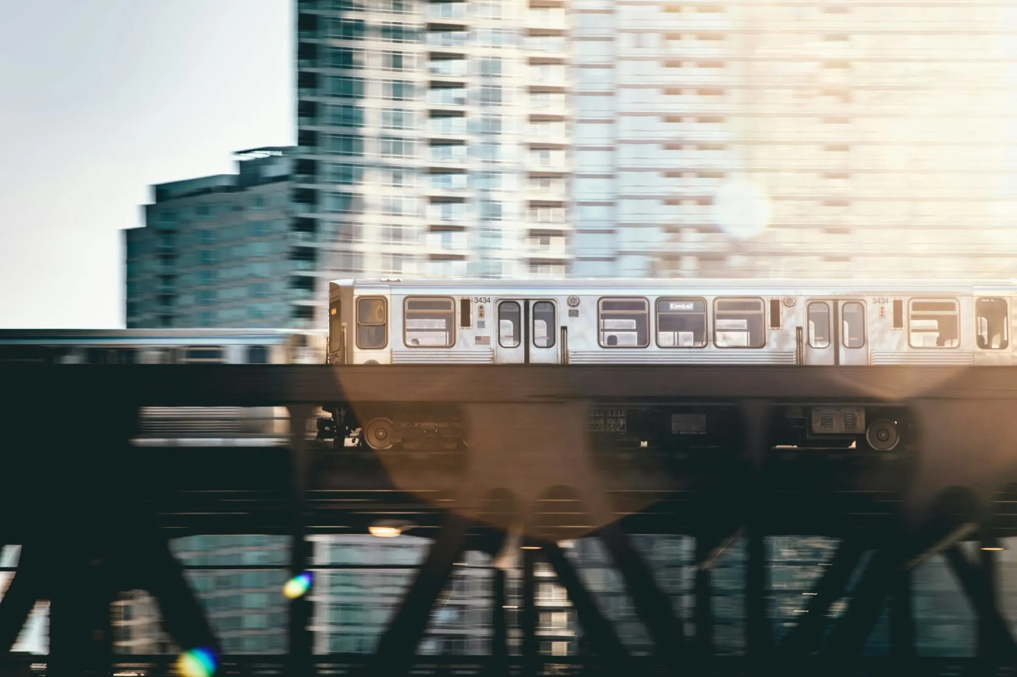 A train speeding past on an elevated track in front of a city skyline during daylight.